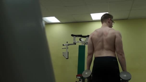 Joven entrena sus hombros con pesas en el gimnasio — Vídeo de stock