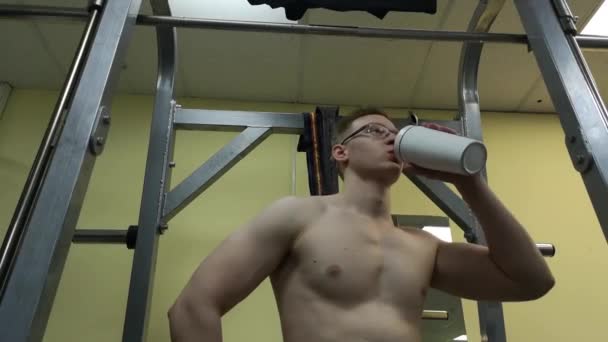 Jovem bebendo água no ginásio. O tipo usa um batido de proteínas. — Vídeo de Stock