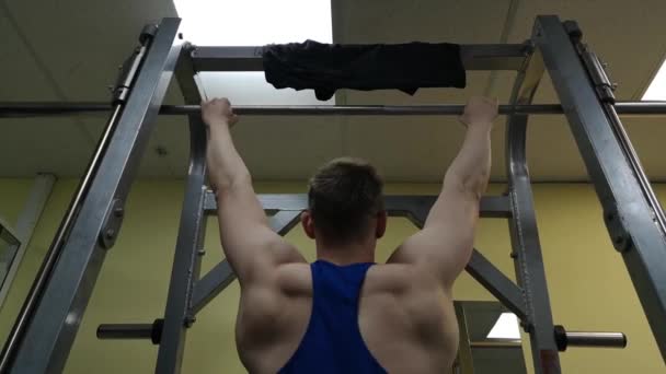 Jonge man houdt zich bezig met fitness in de sportschool. De atleet wordt opgetrokken op de balk — Stockvideo