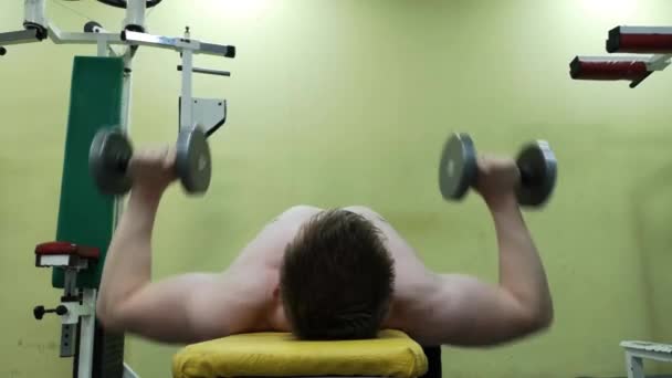 Молодой спортсмен тренирует грудные мышцы в тренажерном зале с гантелями, занимается фитнесом — стоковое видео