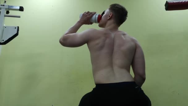 若い男ジムで水を飲む。男はプロテイン シェークを使用します。 — ストック動画