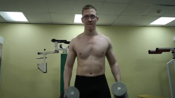Молодой человек тренирует плечи гантелями в спортзале — стоковое видео