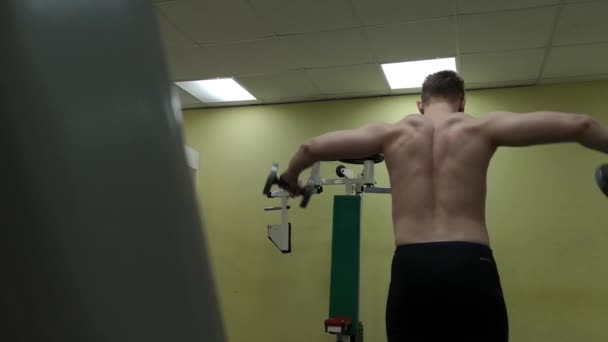 Young man trains his shoulders with dumbbells in the gym — Stock Video