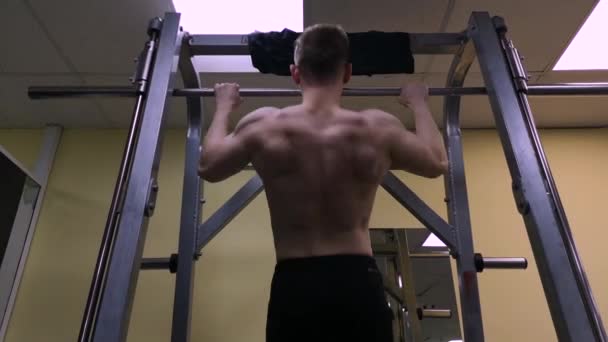 Der junge Mann betreibt Fitness im Fitnessstudio. Der Athlet wird an der Latte hochgezogen — Stockvideo