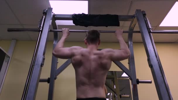 Jonge man houdt zich bezig met fitness in de sportschool. De atleet wordt opgetrokken op de balk — Stockvideo