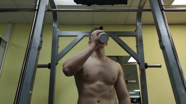 Jovem bebendo água no ginásio. O tipo usa um batido de proteínas. — Vídeo de Stock
