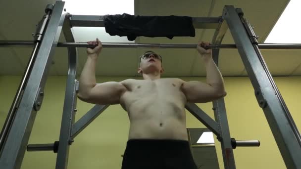 O jovem está envolvido em fitness no ginásio. O atleta é puxado para cima no bar — Vídeo de Stock