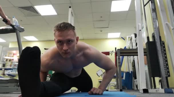 Ung atletisk man värmer upp stretching före utbildningen på golvet i gymmet — Stockvideo