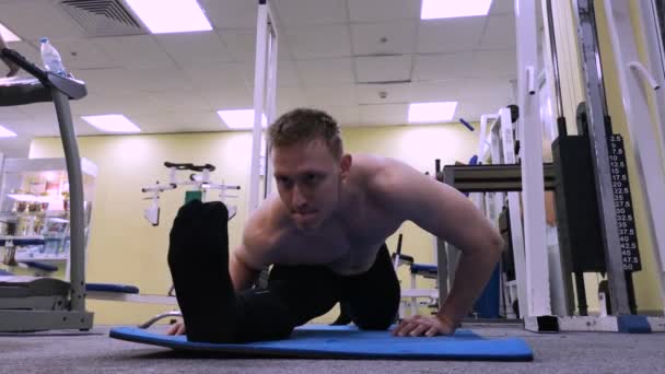 Nuori urheilullinen mies lämpenee venyttely ennen koulutusta lattialla kuntosalilla — kuvapankkivideo
