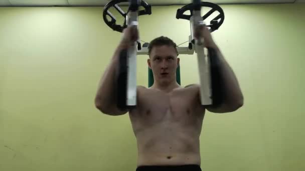 Молодий чоловік тренує грудні м'язи в тренажерному залі, займаючись фітнесом — стокове відео