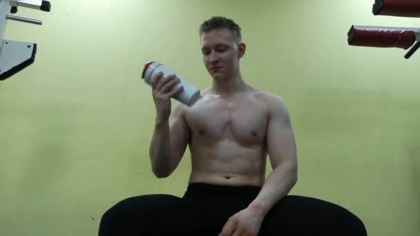 Un joven bebiendo agua en el gimnasio. El tipo usa un batido de proteínas. — Vídeos de Stock