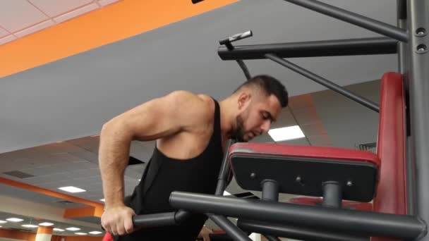 Joven hombre muscular durante el entrenamiento en el gimnasio realiza flexiones en las barras — Vídeos de Stock