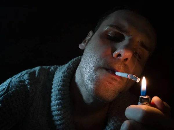 若いの暗いと陰気画像黒の背景に喫煙の男性します。男はタバコを点灯します。 — ストック写真