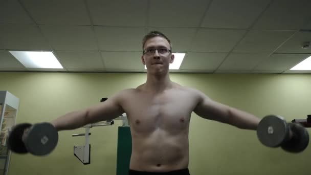 Russland, togliatty - 21. Februar 2019: Junger Mann trainiert seine Schultern mit Hanteln im Fitnessstudio — Stockvideo