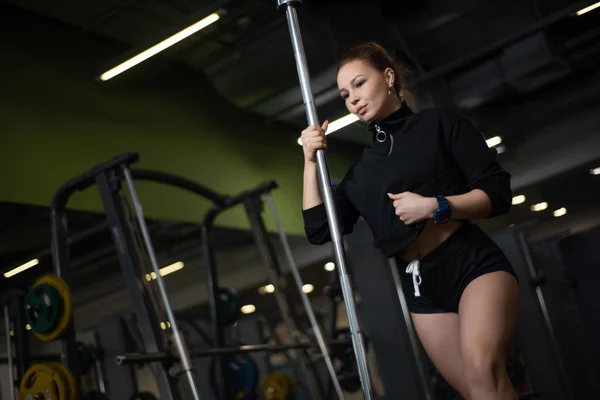 Chica posando en el gimnasio, mostrando su cuerpo, sosteniendo una barra — Foto de Stock