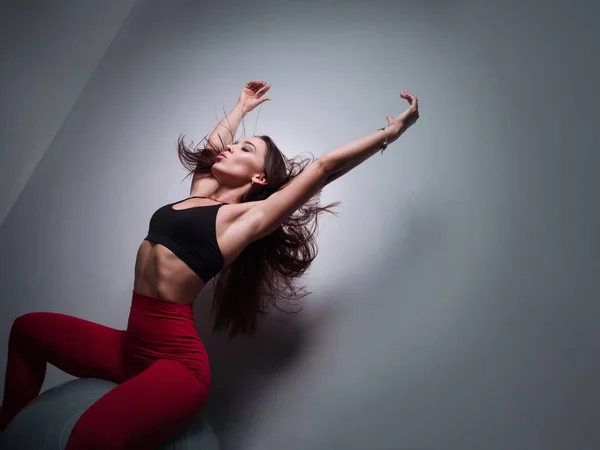 Fitness menina posando em uma bola de ginástica perto da parede, mostrando um corpo e cabelo voador — Fotografia de Stock