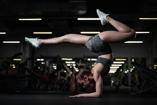 Yogi meisje doet geavanceerde inversie en arm-evenwicht Scorpion Handstand. Vrischikasana. Fitness meisje voert gymnastische element in sportschool — Stockfoto