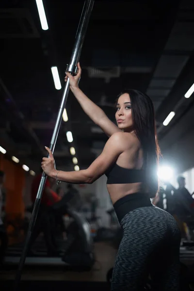Mädchen posiert im Fitnessstudio, zeigt ihren Körper und hält eine Langhantel — Stockfoto