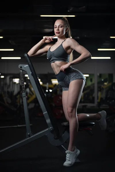 Chica de fitness posando en el gimnasio en el banco mostrando su cuerpo — Foto de Stock