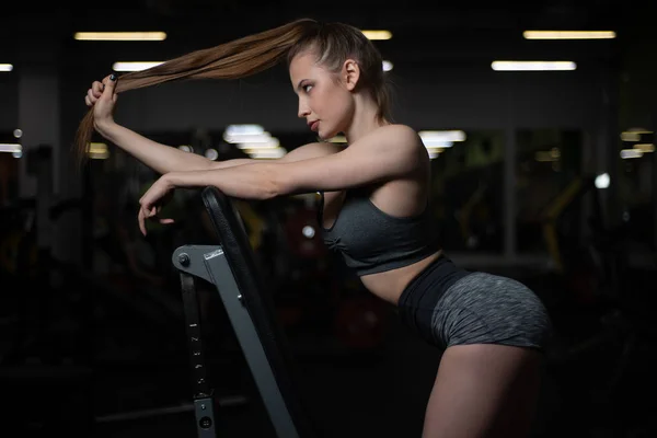 Фитнес-девушка позирует в спортзале на скамейке, показывая свое тело. — стоковое фото