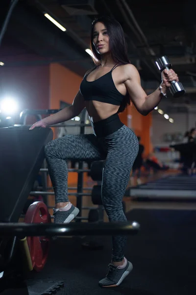 Фитнес-девушка тренирует бицепсы с гантелями в тренажерном зале . — стоковое фото