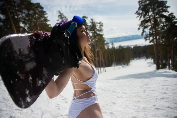 Жінка одягнена в купальник зі сноубордом в руках, дивлячись на відстань. Зимові види спорту — стокове фото