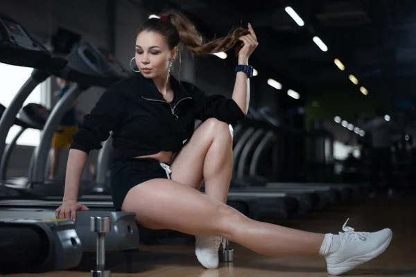 Fitness menina posando no ginásio sentado na esteira, mostrando seus egs Fotos De Bancos De Imagens