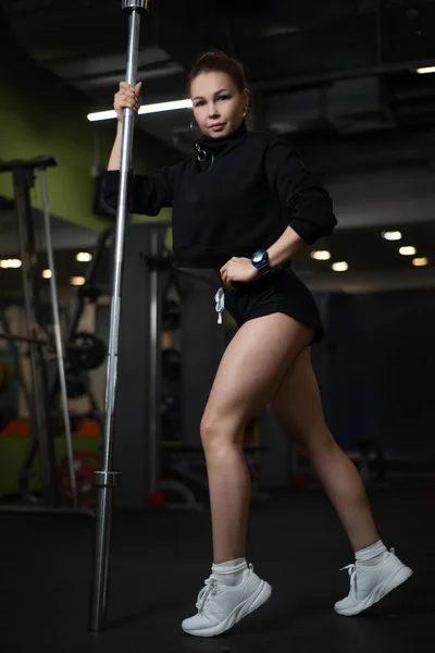 Dziewczyna pozuje w siłowni, pokazując jej ciało, zorganizowanie barbell — Zdjęcie stockowe