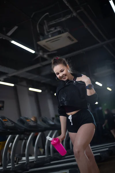 Fitness girl after training drank water in the gym, having fun