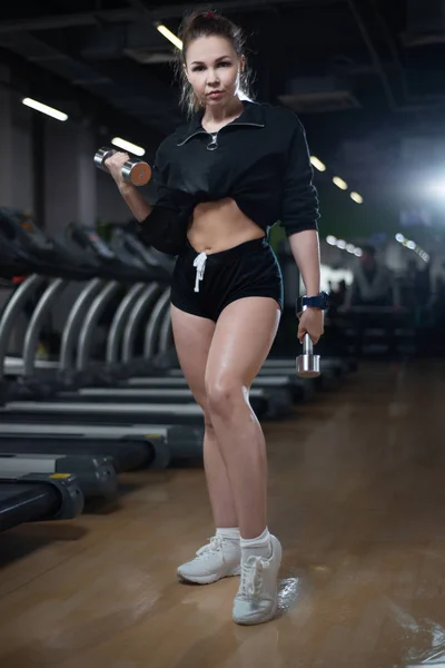 Fitness meisje poseren in de sportschool met halters in haar handen, haar lichaam pronken — Stockfoto