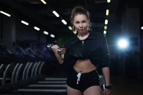 Fitnessmädchen posiert im Fitnessstudio mit Hanteln in den Händen und zeigt ihren Körper — Stockfoto