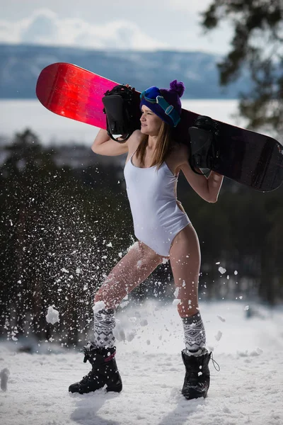 Приваблива жінка, одягнена в купальник, позує зі сноубордом в руках. Зимові види спорту та літаючий сніг — стокове фото