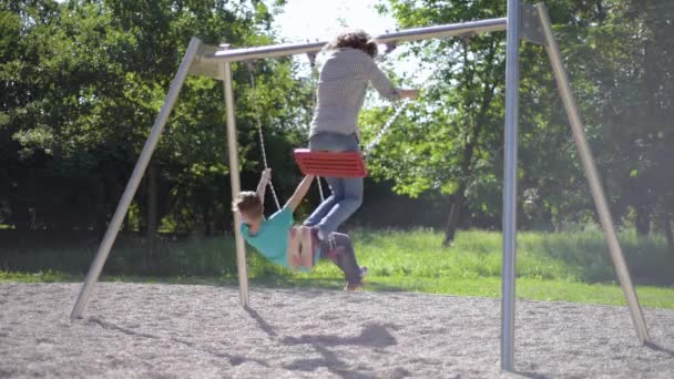 Crianças em baloiços no parque infantil — Vídeo de Stock