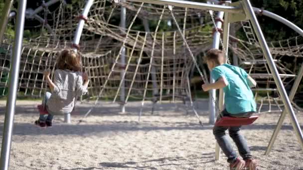Діти на гойдалках на дитячому майданчику — стокове відео