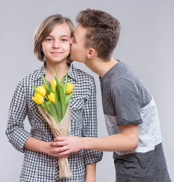 Boy Giving Flowers for Girl. Holidays, Love, Happiness and People concept - Happy Child celebrating Valentines Day. Teen Boy kisses a Girl.