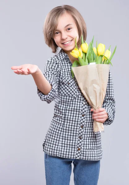 灰色の背景の上に花の束を持つ美しい少女 贈り物として黄色のチューリップの花束と笑顔の子 幸せな母親 誕生日やバレンタインの日 — ストック写真