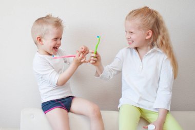 Sevimli küçük sarışın kız ve erkek diş fırçaları. Eğlenceli ev oyun. Çocuk gülümse. Sağlıklı yaşam, dişçi korkmuyorum. Sağlık, diş hijyeni