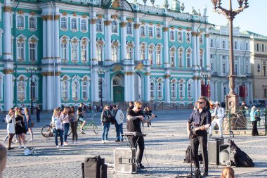 ST. PETERSBURG, RUSSIA - MAY 12, 2018: Street musicians perform for tourists and tips on city center Palace Square. View on State Hermitage museum Winter Palace in Saint Petersburg, Russia clipart