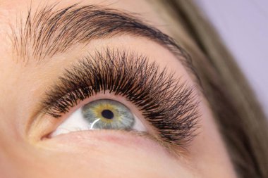 Kirpik uzatma yordamı. Kadın uzun yanlış Eyelashes gözle. Moda gözleri visagein güzellik salonu içinde makro çekim kapatın.