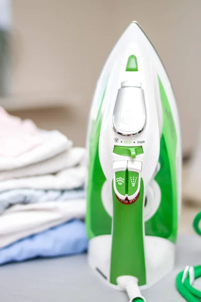 Electric green iron and pile of clothes on ironing board.