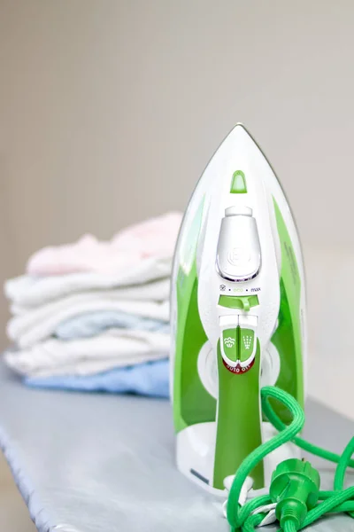 Electric green iron and pile of clothes on ironing board.
