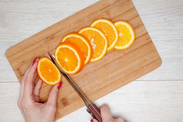 Slice of orange on wooden board. Sharp knife. Woman hands housewife or cook in kitchen slicing fresh citrus orange fruits on cutting board for salad or juicing.