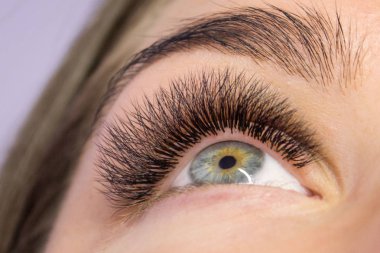 Kirpik uzatma yordamı. Kadın uzun yanlış Eyelashes gözle. Moda gözleri visagein güzellik salonu içinde makro çekim kapatın.