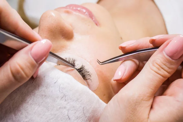 Güzellik ve moda kavramı - kirpik uzatma yordamı. Kadın uzun yanlış Eyelashes gözle. Cımbız üstadı çalışıyor.