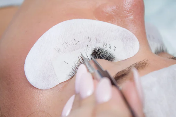 Beauty and fashion concept - Eyelash Extension Procedure. Woman Eye with Long false Eyelashes. Master of tweezers is working.