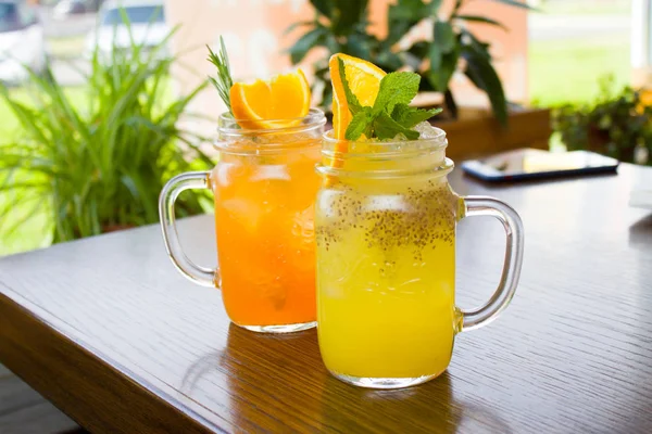 içecekler, insanlar ve yaşam tarzı kavramı - iki taze tropikal sarı ve turuncu Alkolsüz kokteyl ile chia tohum turuncu ve nane dilim ile dekore edilmiş bir mason kavanoza