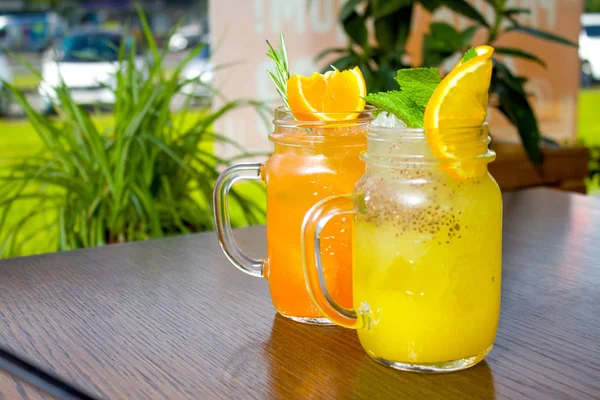içecekler, insanlar ve yaşam tarzı kavramı - iki taze tropikal sarı ve turuncu Alkolsüz kokteyl ile chia tohum turuncu ve nane dilim ile dekore edilmiş bir mason kavanoza