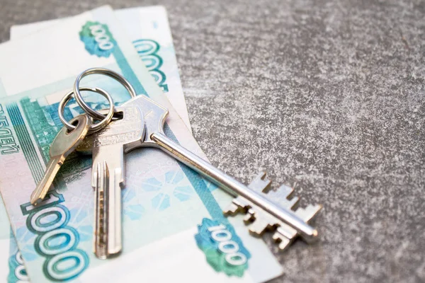 finance, rental and new home concept - bundle of money Russian Banknotes thousand rubles and three House Keys on concrete background. Copyspace