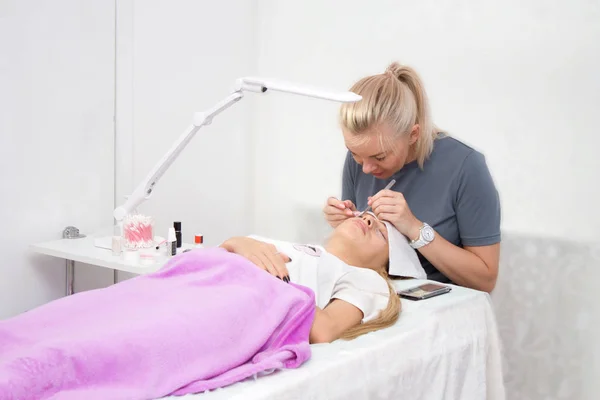 Güzellik ve moda konsepti-kirpik uzatma prosedürü. Cımbız ustası kadın göz uzun yanlış kirpik için salon yapımında çalışıyor.