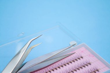 Güzellik ve moda kavramı - kirpik uzatma yordamı için araçlar. İki cımbız ve mavi arka plan üzerinde sahte kirpikleri kutusuyla. boşaltmak mockup